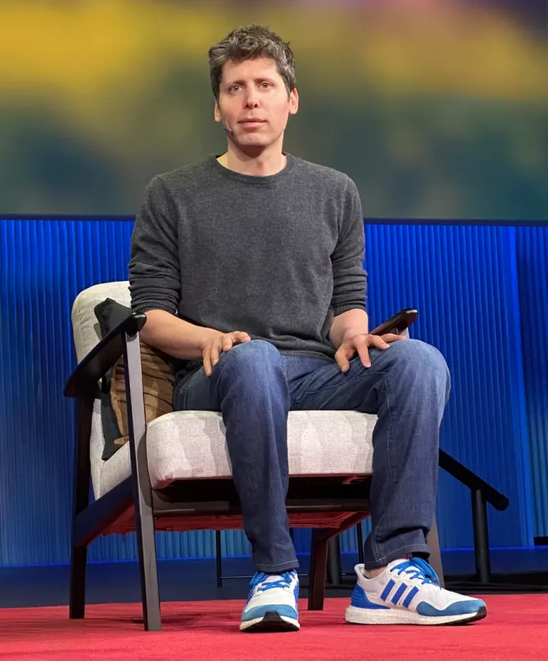 Sam Altman seduto in poltrona a TED nell’aprile 2025, con la figura intera e le scarpe visibili