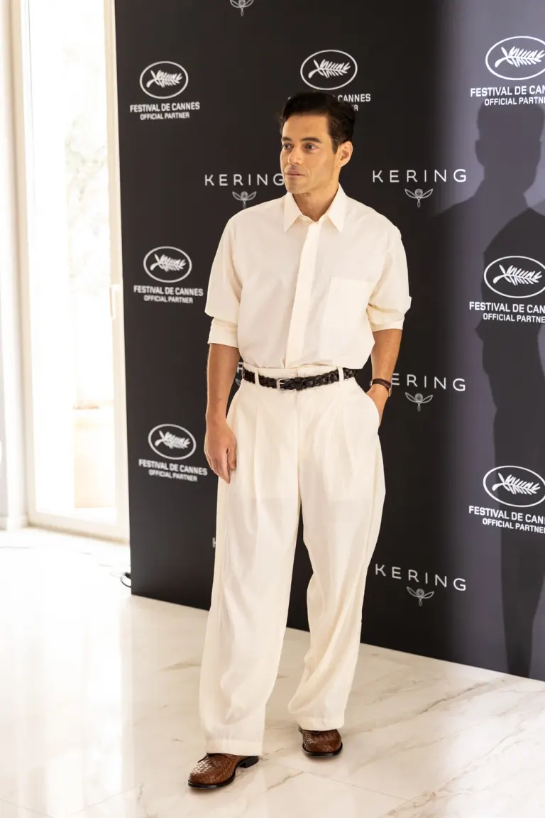 Foto a figura intera di Rami Malek in camicia bianca e pantaloni a un photocall di Cannes nel maggio 2026