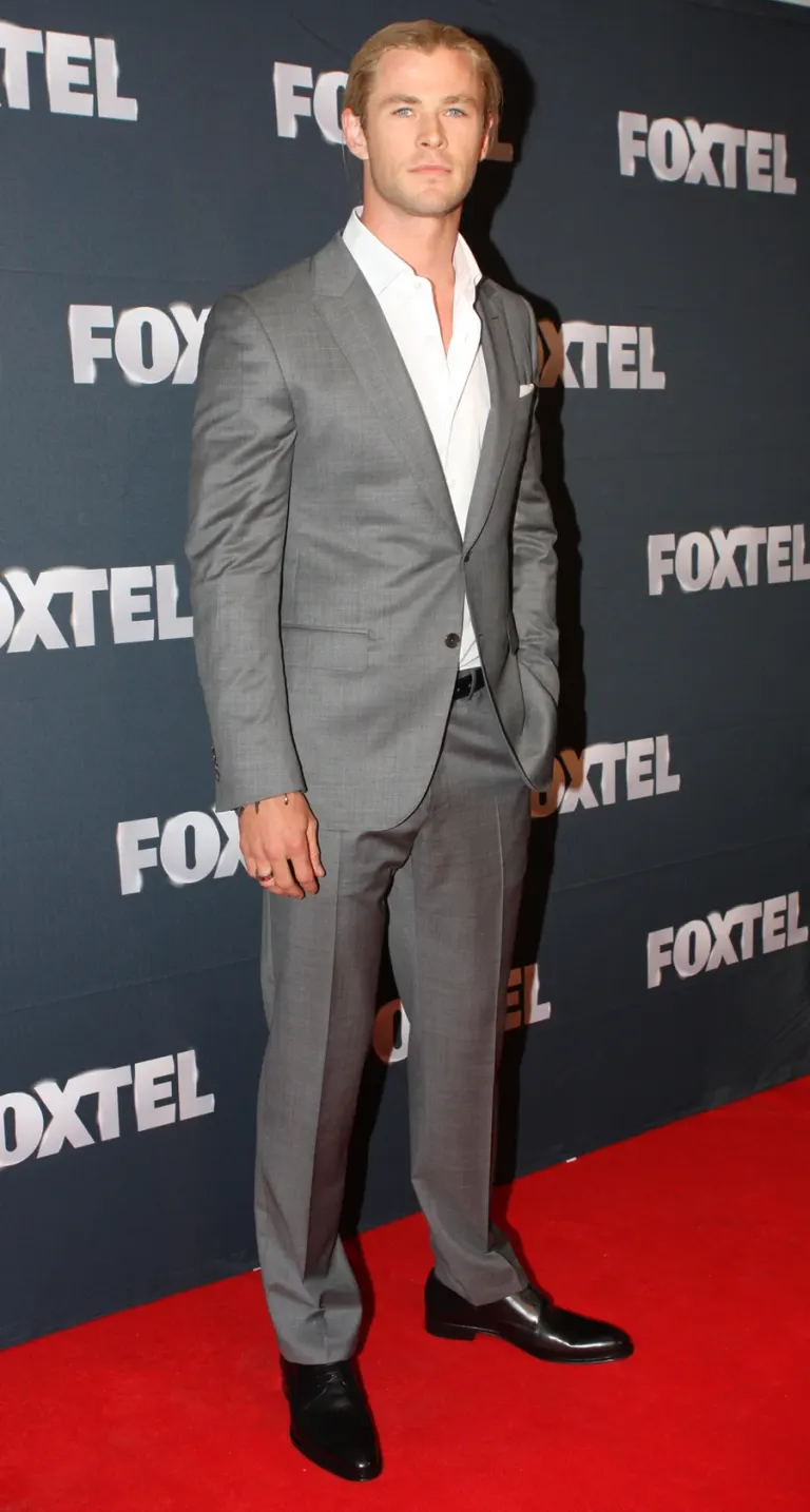 Chris Hemsworth photographié en pied, posant en costume gris sur un tapis rouge devant un fond Foxtel en février 2013